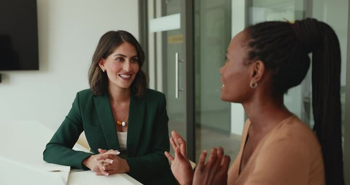 Smiling Hispanic woman speaking with colleague or client, consulting, provide explanations looking engaged and interested in conversation. Two workmates met in office for exchanging opinions or ideas