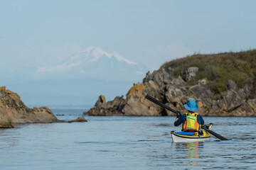 Woman kayaking along Sucia Island in the San Juan Islands in the Pacific Northwest in Washington with Mt Baker in background