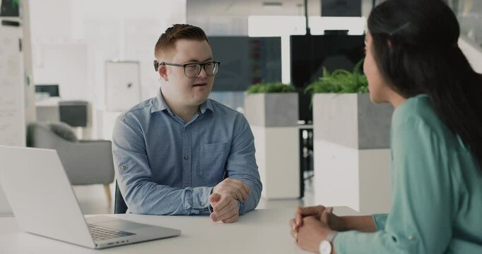Man with Down syndrome lead talk with female colleague or client seated at desk in modern office, shake hands finalizing formal meeting, negotiations, express recognition for getting professional help