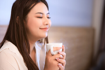 asian woman sitting on bed drinking coffee at morning time