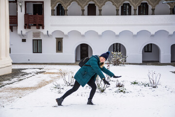 Young woman traveler sliding playfully on snowy ground near horezu monastery, capturing winter...