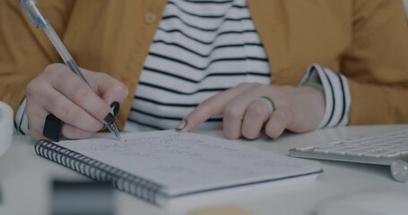 Close-up of female hand writing business ideas in notebook and working with computer at desk in office. Job and businessperson concept.