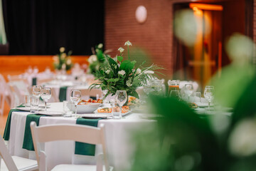 Elegant table setup with floral centerpiece, glassware, and white tablecloths at a banquet event, captured through blurred greenery.