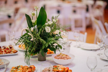 A table centerpiece with green and white floral arrangement surrounded by plates of food and glassware in an elegant banquet setting.