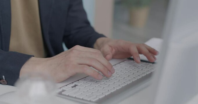 Close-up of male hands typing with computer keyboard at desk in office. Businessman working online sitting at table in workplace with modern device.
