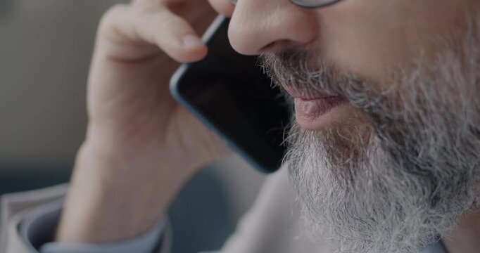 Close-up of man speaking on mobile phone against blurred office background. Cellphone communication and modern technology concept.