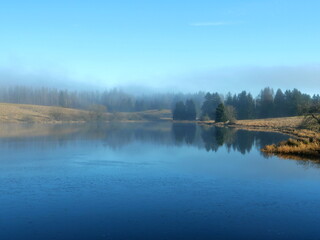 Obraz premium A mystical mining pond in the Harz. Fog, reflections, and horizons in winter create an enigmatic atmosphere, perfect for diverse themes.