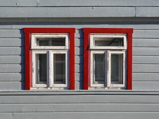 Photo of a gray wooden facade with two windows with red frames. The inspiring color composition of gray and red is ideal for design projects.