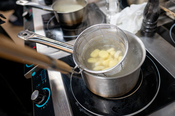 A close-up of a stainless steel pot on a modern stove, with a colander holding cooked dumplings being submerged in boiling water. Steam rises, creating a cozy kitchen atmosphere.