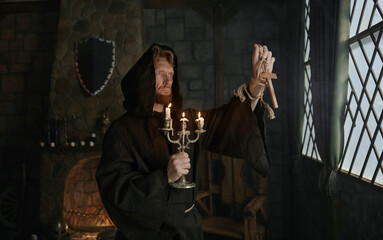 Portrait of hooded monk in medieval costume holding wooden cross and candlestick