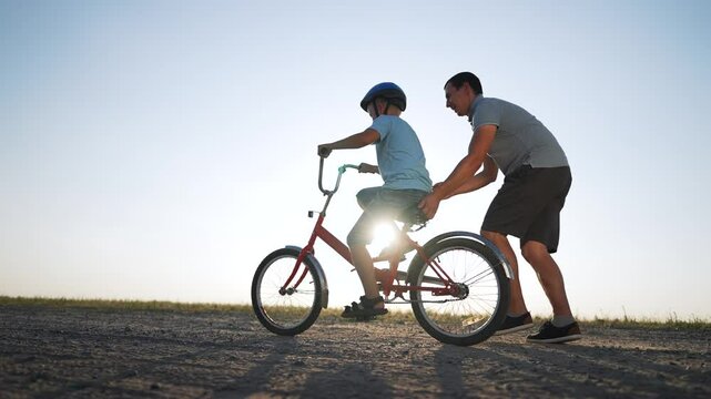 Father's Day. Father teaches son to ride bicycle wearing safety helmet. child learn to ride bicycle in park at sunset. Happy family concept and dream. Active father teaches child to ride bike in park