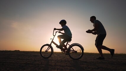Father's Day. Father teaches son to ride bicycle wearing safety helmet. child learn to ride bicycle...