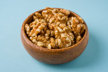 Top view of heap of walnut kernels in wooden bowl on blue background