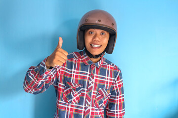 Young Asian man wearing motorbike helmet giving "thumb up" fingers sign