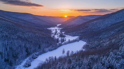 Sunset over snow-covered valley with river winding through forested mountains