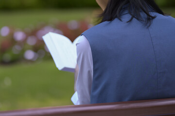 公園のベンチに座って読書をする女性