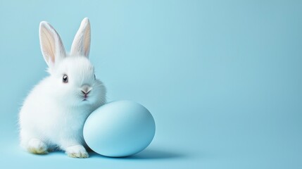 Fototapeta premium Adorable White Bunny with a Blue Easter Egg on a Soft Blue Background