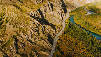 Aerial view of a scenic highway winding through a dramatic mountain valley, following the curves of a turquoise river, amidst colorful autumn foliage