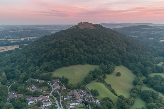 Aerial view of a lush green hill at sunset, overlooking a quaint village. Serene landscape photography.