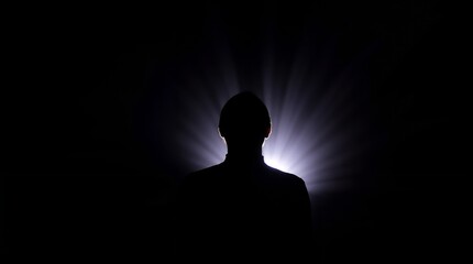 Esoteric silhouette of a person with glowing light rays behind in a dark environment