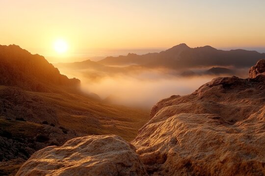 Spectacular sunrise over misty mountains with rocks in foreground captured during early morning hours