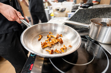 A chef skillfully pans sautéing golden chanterelle mushrooms in a professional kitchen, showcasing...