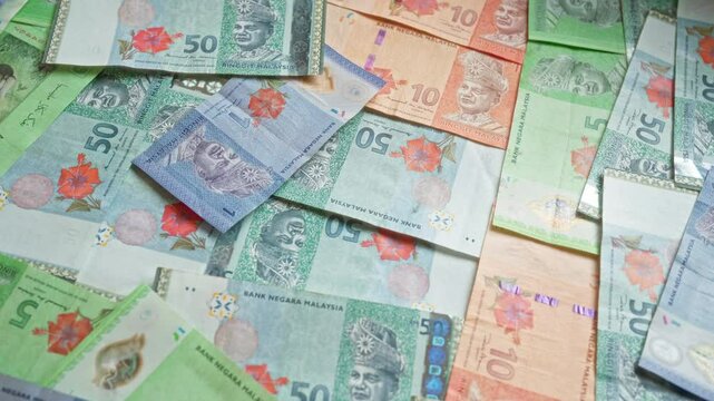 Malaysian banknotes of various denominations, including 1, 5, 10, and 50 ringgit, are scattered on a surface showcasing malaysia's currency.