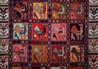 Traditional rug with intricate geometric patterns in red, orange, yellow, pink, and black. Symmetrical shapes and vibrant colors create a rich tapestry design, bordered by bold, contrasting edges.