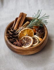 Fototapeta premium Wooden bowl holding dried orange slices, cinnamon sticks, pine cone, and evergreen sprig creating cozy winter atmosphere
