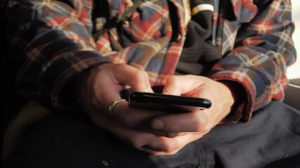 Man in vintage flannel shirt typing message on smartphone for social media in public transport, close-up. Hands using chat or messaging app on mobile phone. Searching for information on Internet.