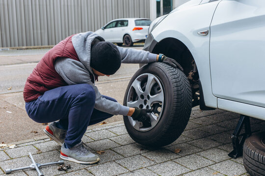 Man using a wrench to replace his car's tire, switching to winter tires for the cold season