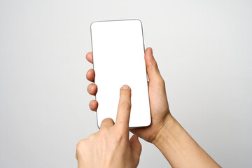 Finger touching phone on white background with copy space. Woman holding smartphone with white screen. Hand tap blank cellphone display, close-up