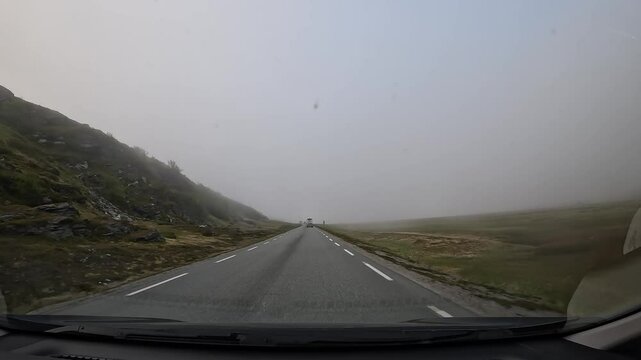Driving through the tundra in northern Norway on E69 road. Surrounded by rocks and low grass. Foggy atmosphere creates a mysterious and serene landscape.