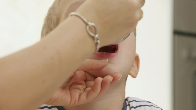 Woman giving liquid medicine to child in tablespoon