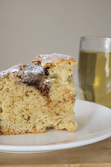 A piece of cake with chocolate chips on a plate and tea in a glass goblet.