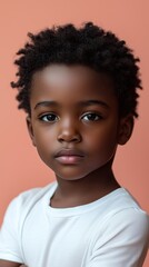 Close-up portrait of a young child against a peach background, wearing a white shirt, with a thoughtful expression.