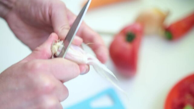 close up of unrecognizable male hands chopping garlic on board. Man's hands cutting garlic with a knife over cutting board. Making food at home, homemade