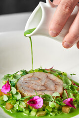 Dish featuring a delicate piece of fish, surrounded by a vibrant arrangement of fresh vegetables and edible flowers. The plate is garnished green sauc