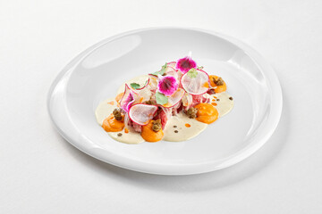 A gourmet dish featuring a delicate piece of venison steak, surrounded by a vibrant arrangement of fresh vegetables and edible flowers