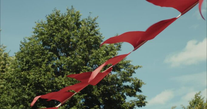 Red flags waving in the wind against blue sky and green tree