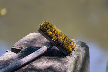 Ruda Milicka / Poland: Wooden scrubber with yellow bristles on the concrete edging of a small side weir on the Pradni River