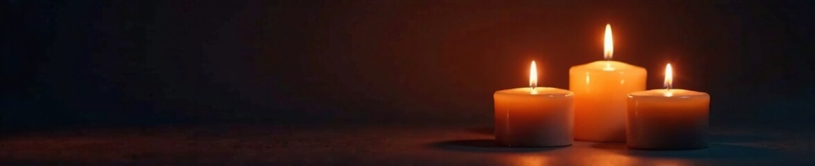 Soft warm glow of three burning candles on a dark background, abstract, shadows, light