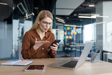 Upset and disappointed woman sitting inside office with phone in hands, businesswoman received...