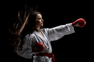 girl exercising karate punch wearing kimono and red gloves against black background © Nikola Spasenoski