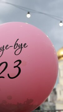 Pink balloon with 'Bye-bye 23' against cloudy sky, golden dome in background, festive celebration atmosphere concept