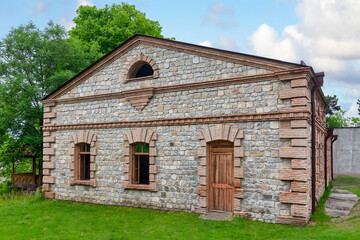 Obraz premium Constructed from stone and brick, this historic building features large windows and a wooden door, set against lush greenery under a bright sky, showcasing its architectural elegance