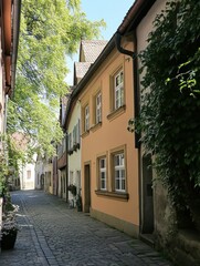 Fototapeta premium A charming cobblestone lane lined with pastel-colored buildings and lush greenery on a bright sunny day, creating a peaceful European atmosphere