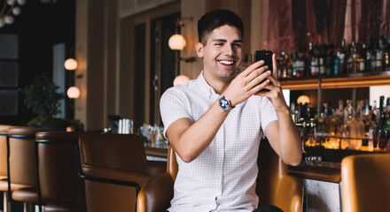 Happy man taking shot with smartphone while sitting at counter
