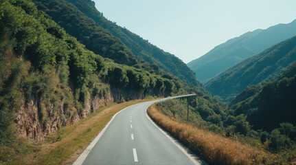 Fototapeta premium Winding road through lush green mountains on a sunny day in a serene landscape