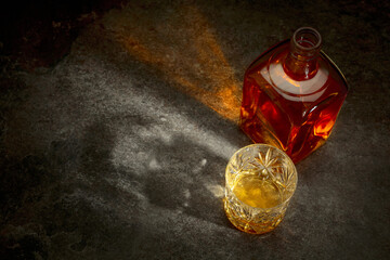 Bottle and crystal glass of whiskey on a stone table.
